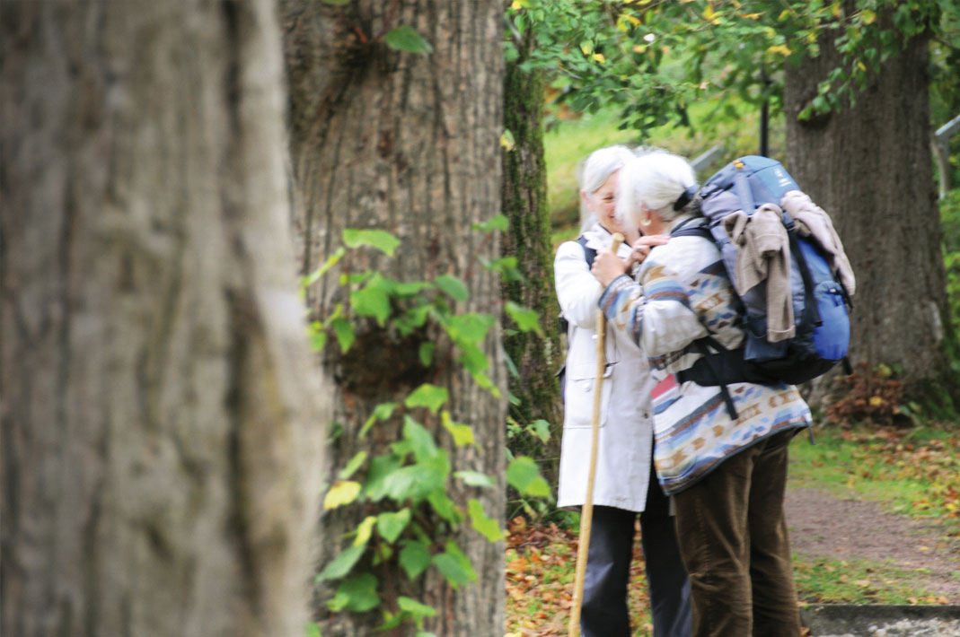 Zwei ältere Pilgerinnen auf Waldweg sind sich zugetan